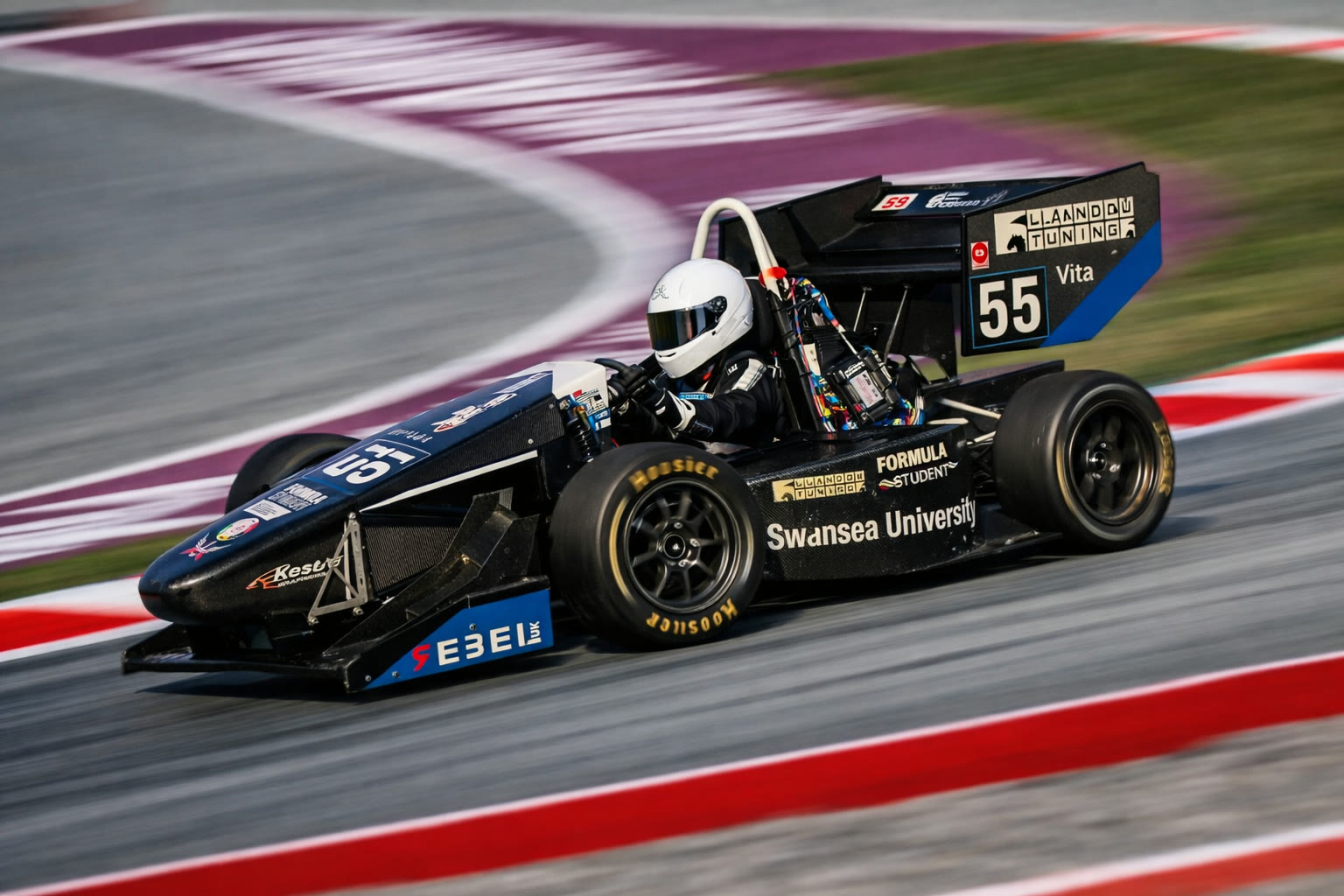 Swansea University Race Engineering number 55 Formula Student car at speed on circuit with Llandow Tuning displayed on the rear wing
