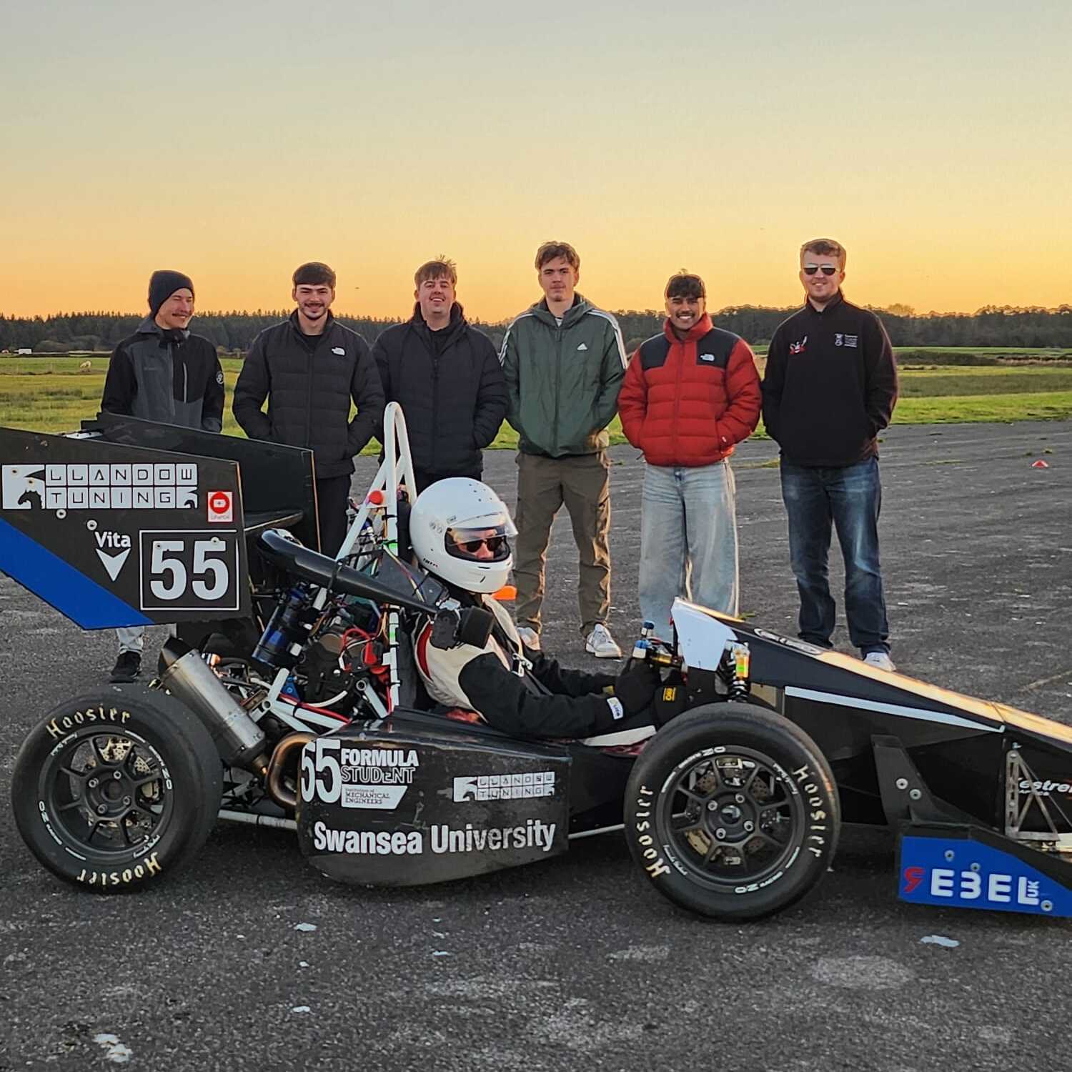 Swansea University Race Engineering students standing with the number 55 Formula Student car during an evening test session